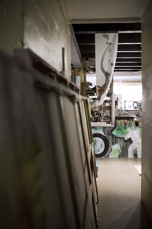 looking down a hallway, stretched canvases on one side, my office straight ahead with a bright green abstract painting in front of the desk